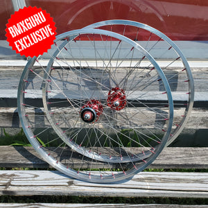 Bicycle wheels with red hub on a wooden surface, featuring 'BMXGURU EXCLUSIVE' label.