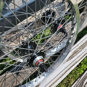 Close-up of a bicycle wheel with metal rim and spokes on a wooden surface.