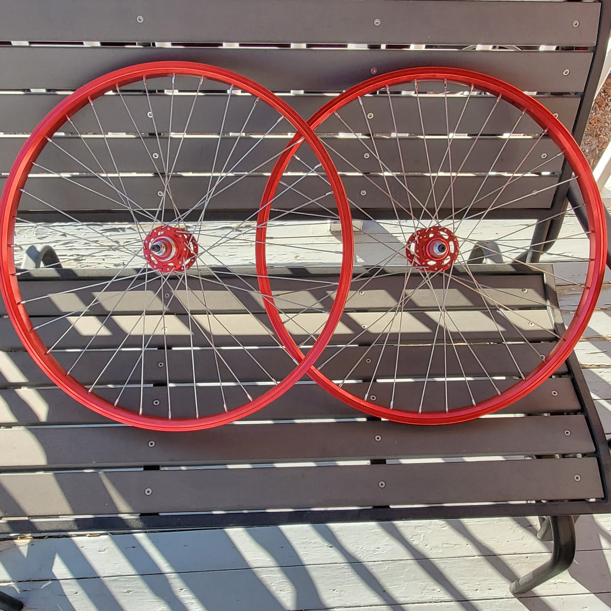 Two red bicycle wheels leaning against a wooden fence.
