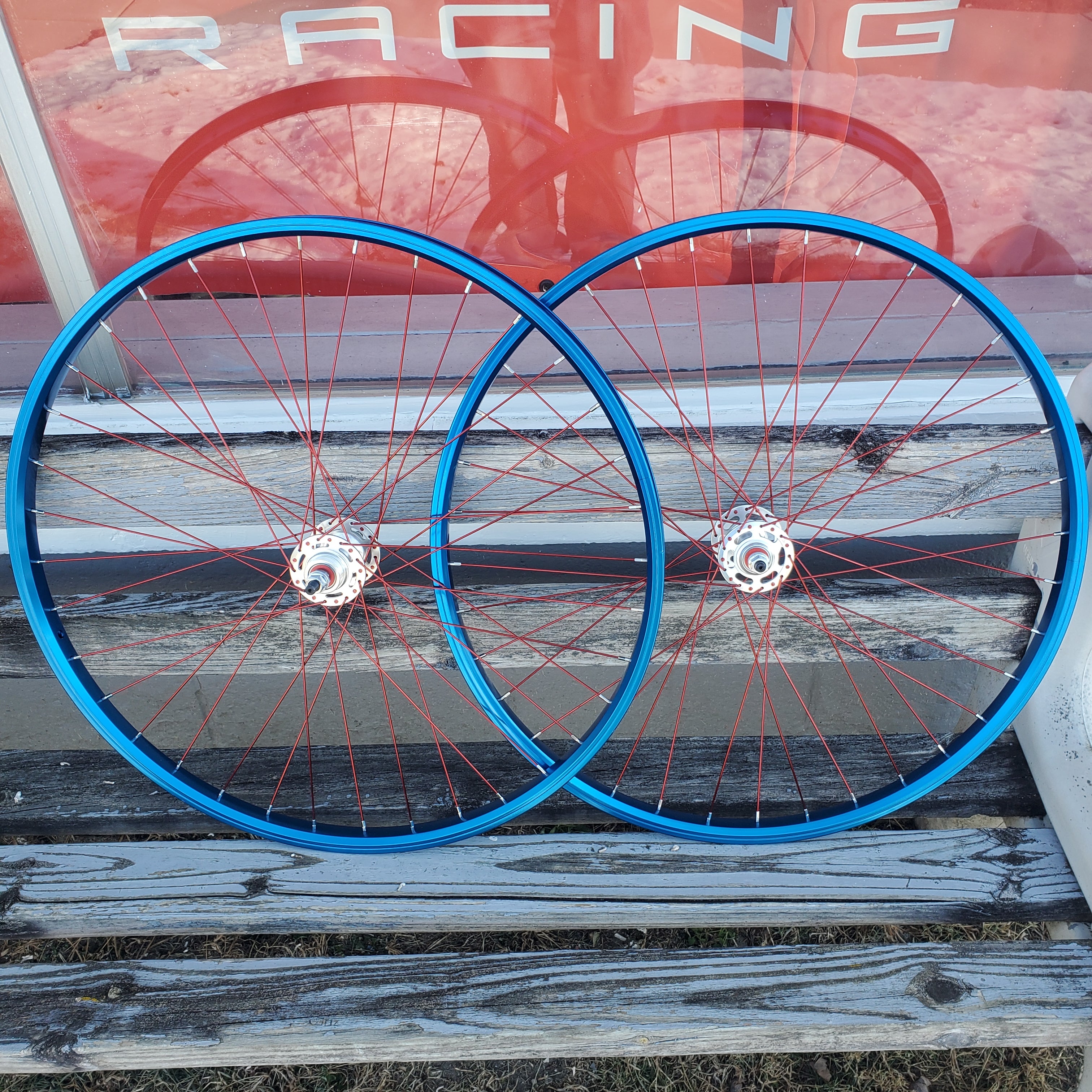 Two bicycle wheels with blue rims and red spokes against a wooden background.