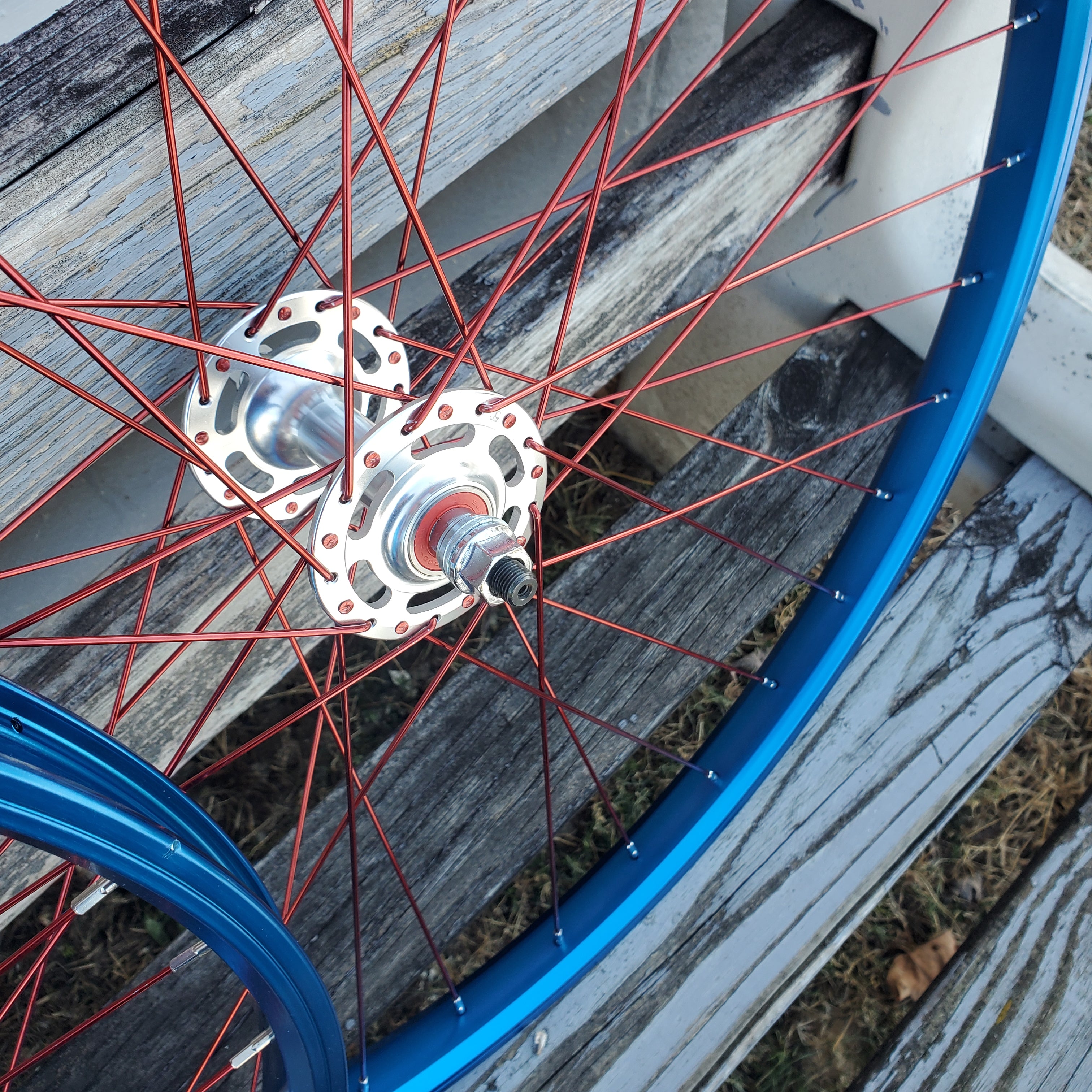 Close-up of a bicycle wheel with red spokes and blue rim on a wooden surface.