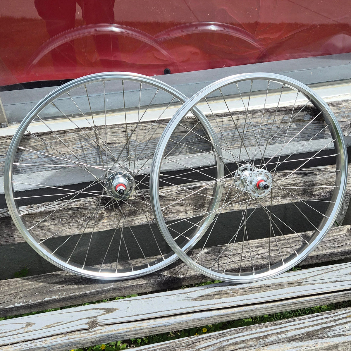 Two bicycle wheels leaning against a wooden fence with a red sign in the background.