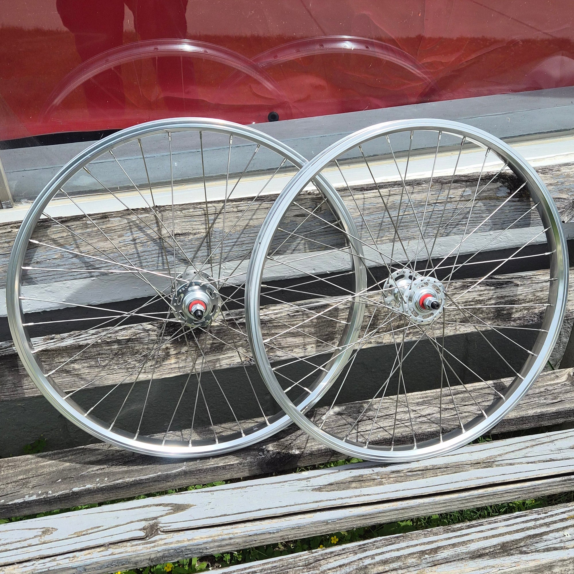 Two bicycle wheels leaning against a wooden fence with a red sign in the background.