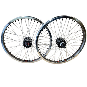Two bicycle wheels with silver rims and spokes, black hubs, and small red and white decals, displayed against a brown cardboard background.