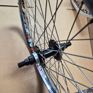 Close-up of a bicycle wheel hub, spokes, and rim resting on a brown cardboard surface.