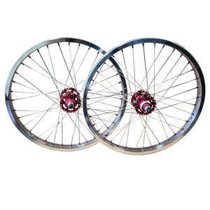 Two bicycle wheels with silver chrome rims and spokes, featuring red hub centers, displayed against a brown cardboard background.
