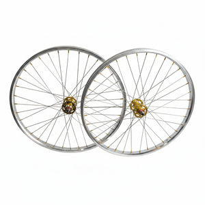 Two bicycle wheels with silver rims and spokes, featuring gold-colored hub centers, displayed against a plain light gray background.