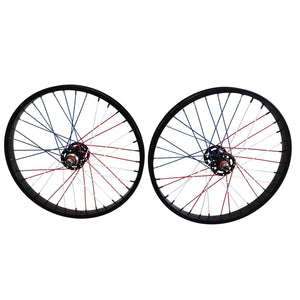 Two bicycle wheels with black rims, black hubs, and blue and red spokes, displayed side-by-side on a light gray background.