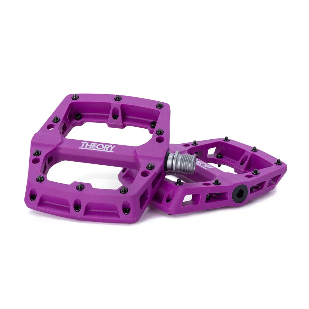 A pair of purple Theory brand platform pedals for bicycles, featuring removable pins and a cro-mo steel axle.